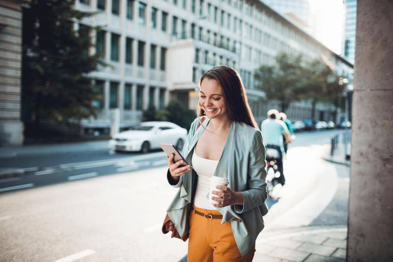 Young woman with smartphone and coffee in city street