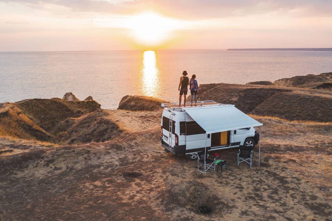 Camper am Meer mit zwei Menschen auf dem Dach 