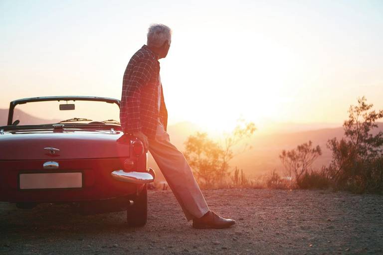 Mann lehnt an seinem Oldtimer im Sonnenuntergang