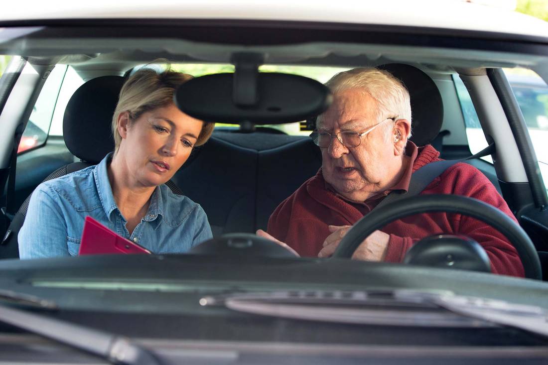 Älterer Mann sitzt im Fahrschulauto mit Fahrtrainerin